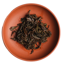 Dried tea leaves in a terracotta bowl on a white background